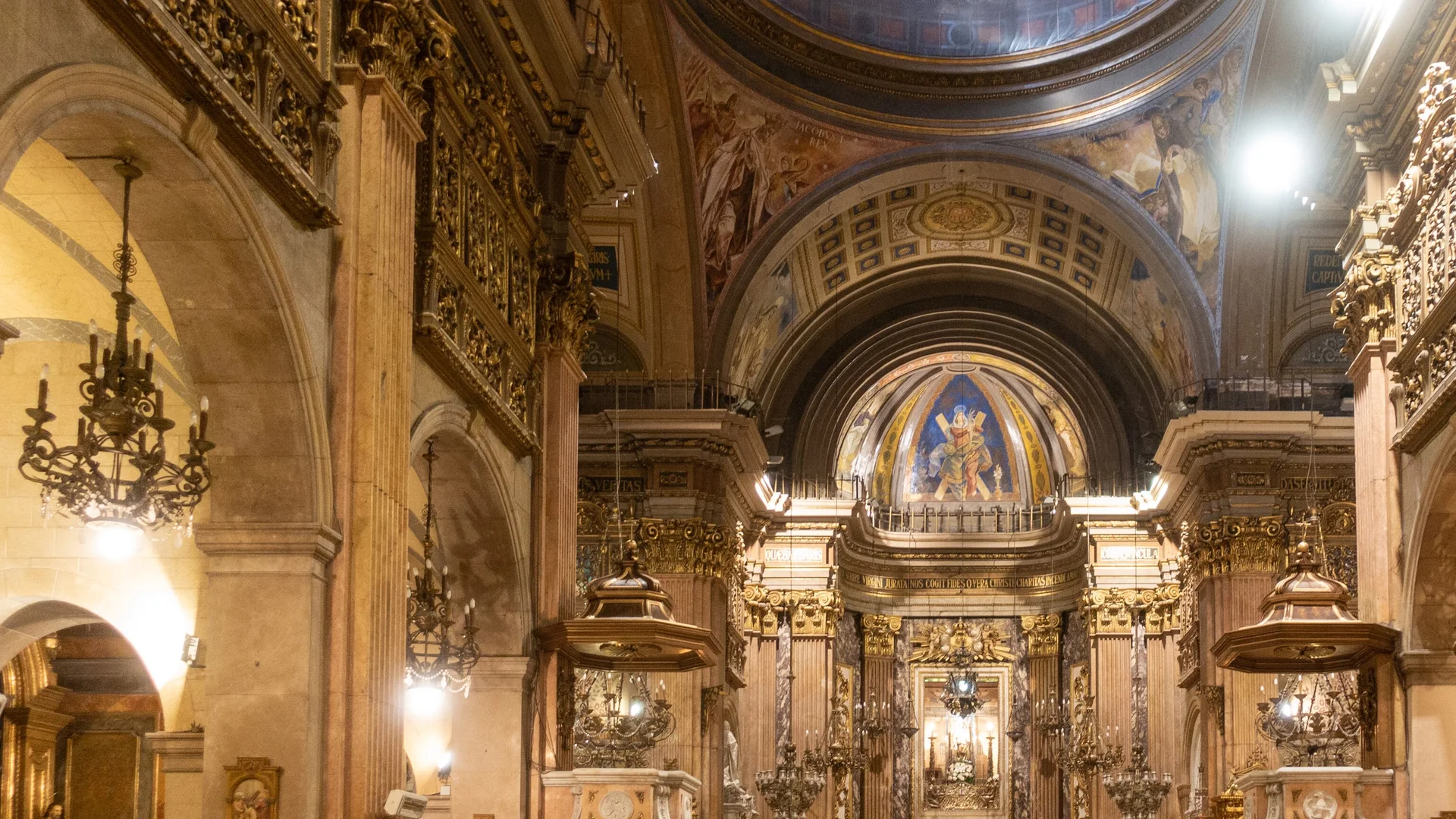 The nave of the Basílica de la Mercè in Barcelona, looking towards the high altar beneath a painted dome, with gilded galleries and hanging lamps on either side
