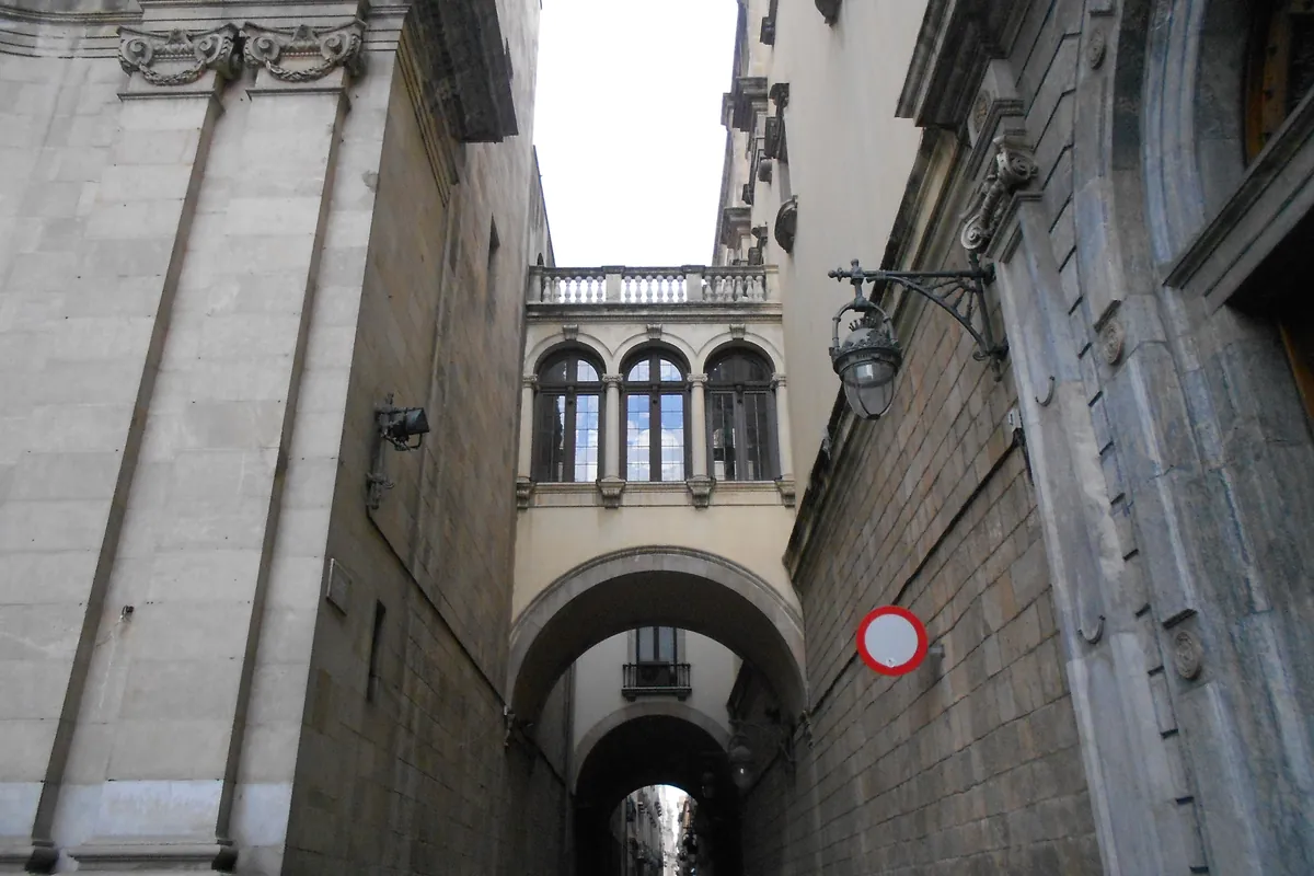 A narrow stone lane in the Gothic Quarter with a covered bridge overhead.