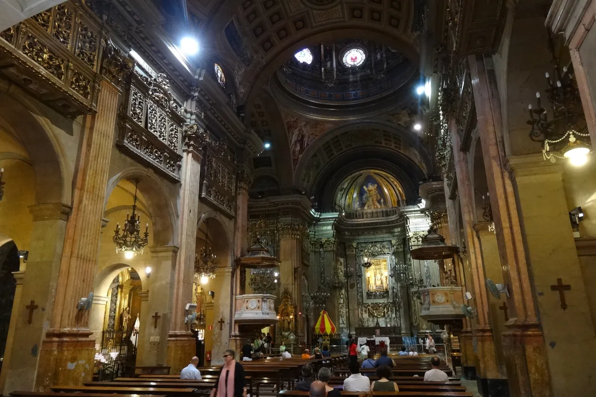 A side view of the nave with pews, chandeliers and gilded galleries.
